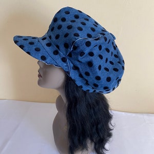 May include: A blue denim hat with black polka dots. The hat has a curved brim and a decorative bow on the side. The hat is displayed on a mannequin head with black hair. The hat is a stylish accessory.