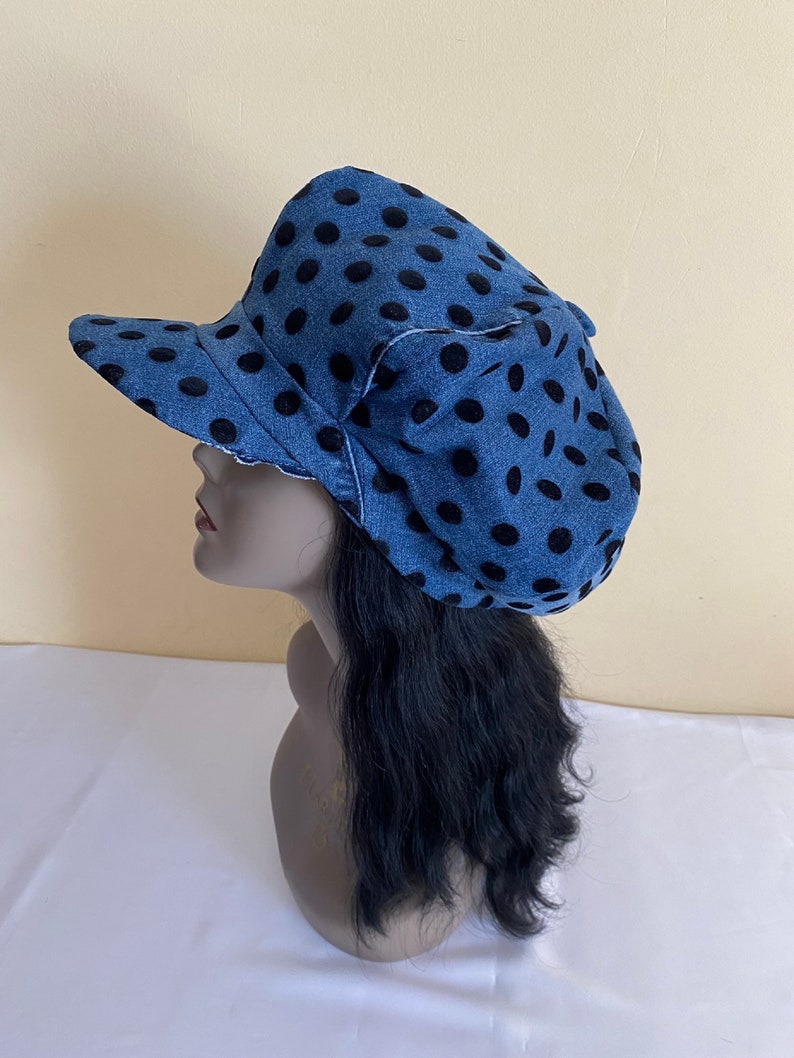May include: A blue denim hat with black polka dots. The hat has a curved brim and a decorative bow on the side. The hat is displayed on a mannequin head with black hair. The hat is a stylish accessory.
