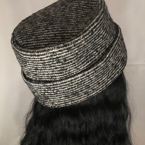 May include: A black and white tweed hat with a horizontal striped pattern. The hat has a rounded top and a band around the base. The hat is a neutral color and can be worn with many outfits.