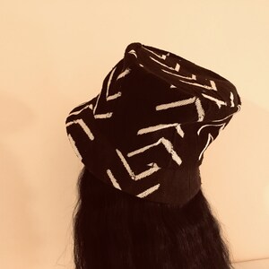 May include: A black hat with a white geometric pattern. The hat has a brim and a crown, and the pattern consists of white lines arranged in a repeating design. The hat is worn on a person's head.