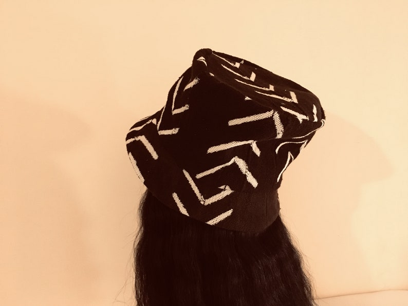 May include: A black hat with a white geometric pattern. The hat has a brim and a crown, and the pattern consists of white lines arranged in a repeating design. The hat is worn on a person's head.