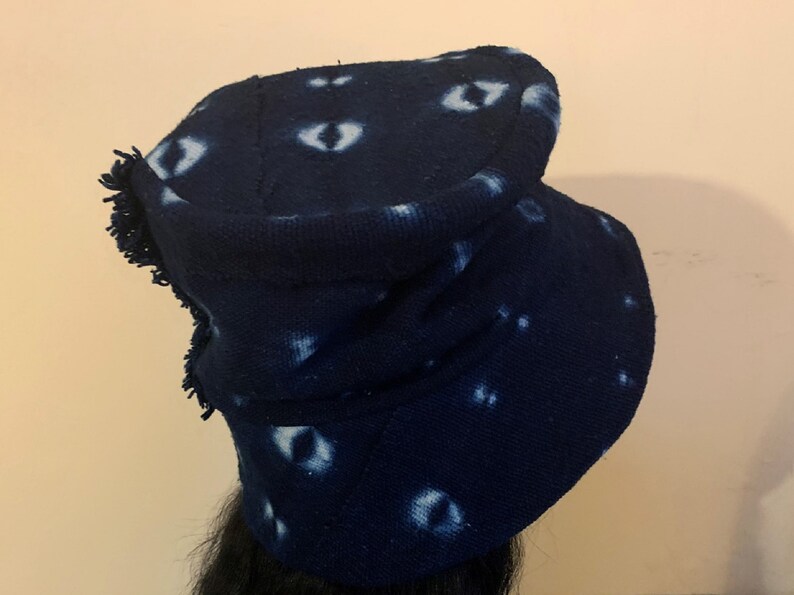 Puede incluir: Un gorro de punto azul marino con un patr&oacute;n &uacute;nico de formas blancas en forma de ojo. El gorro tiene un borde con flecos y un borde doblado. El gorro est&aacute; hecho de una tela suave y texturizada, y es un accesorio elegante para el clima fr&iacute;o.