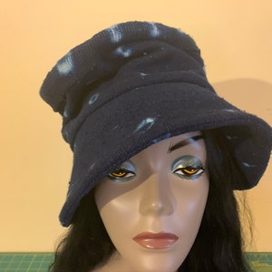 Puede incluir: Un sombrero de pescador azul marino con manchas blancas te&ntilde;idas. El sombrero est&aacute; hecho de una tela suave y texturizada y tiene un ala ancha. El sombrero se muestra en una cabeza de maniqu&iacute; con cabello oscuro.