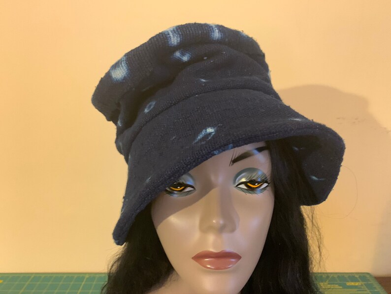 Puede incluir: Un sombrero de pescador azul marino con manchas blancas te&ntilde;idas. El sombrero est&aacute; hecho de una tela suave y texturizada y tiene un ala ancha. El sombrero se muestra en una cabeza de maniqu&iacute; con cabello oscuro.