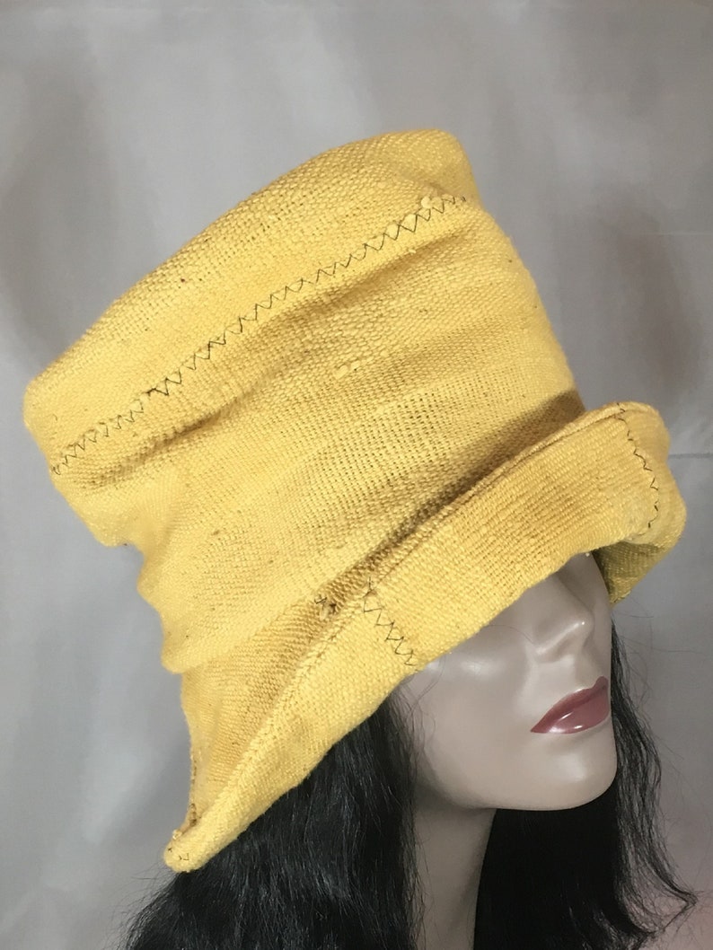 May include: A yellow, textured hat with a brim and a tall crown. The hat has a stitched design along the seams. The hat is displayed on a mannequin head with dark hair.