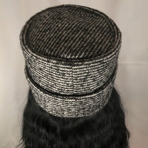 May include: A black and white patterned hat with a cylindrical crown and a brim. The hat has a textured appearance, with a diagonal stripe pattern in shades of black and white. The hat is a stylish accessory.