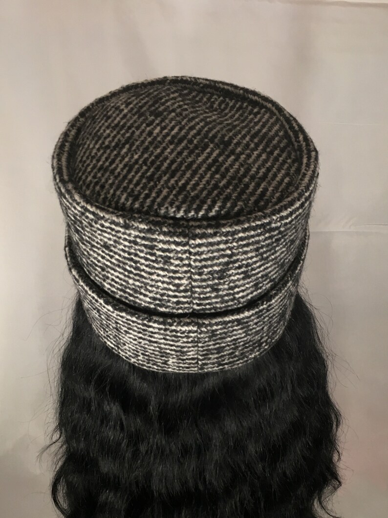 May include: A black and white patterned hat with a cylindrical crown and a brim. The hat has a textured appearance, with a diagonal stripe pattern in shades of black and white. The hat is a stylish accessory.