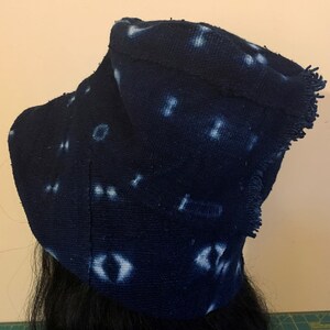 Puede incluir: Un sombrero de tela azul oscuro con patrones de puntos blancos irregulares. El sombrero tiene un borde con flecos y est&aacute; hecho de un material texturizado. El sombrero es probablemente hecho a mano y tiene un dise&ntilde;o art&iacute;stico &uacute;nico.