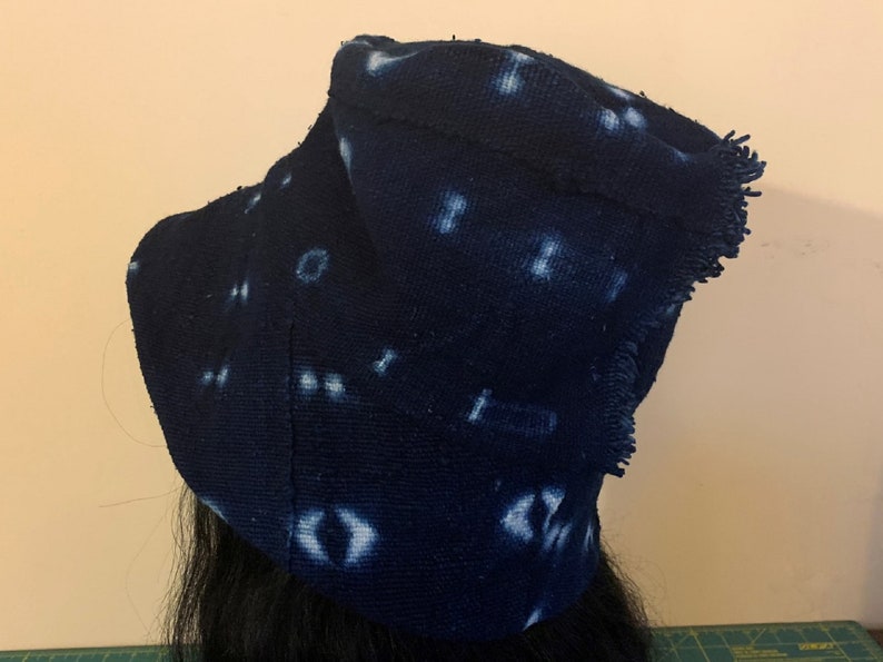 Puede incluir: Un sombrero de tela azul oscuro con patrones de puntos blancos irregulares. El sombrero tiene un borde con flecos y est&aacute; hecho de un material texturizado. El sombrero es probablemente hecho a mano y tiene un dise&ntilde;o art&iacute;stico &uacute;nico.