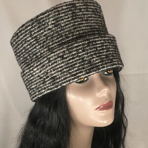 May include: A black and white patterned hat with a wide brim. The hat has a textured appearance and is made of a woven material. The hat is worn by a mannequin with black hair.