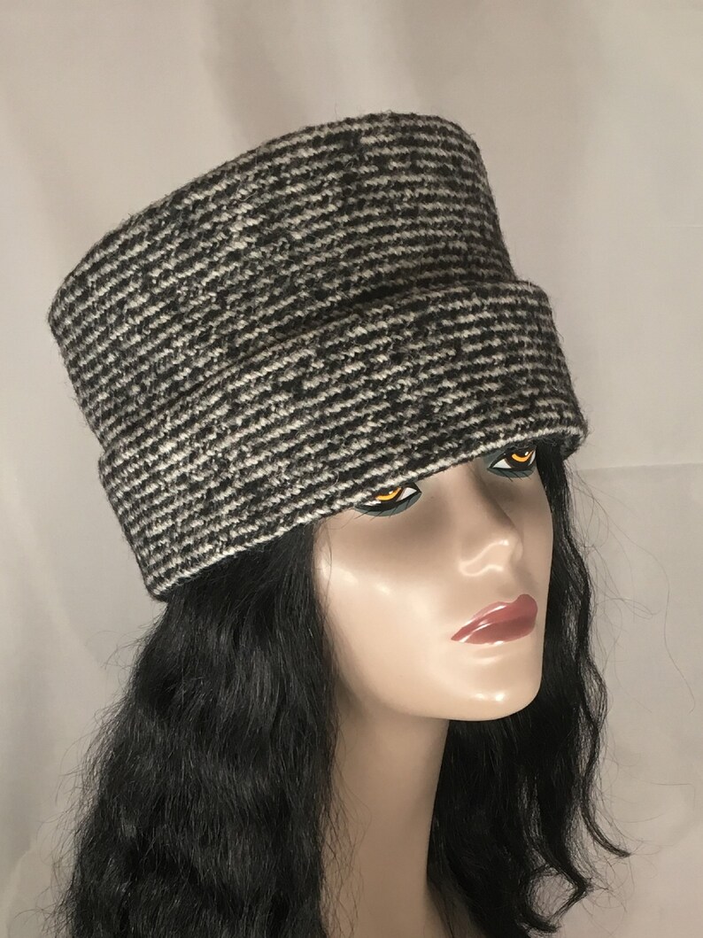 May include: A black and white patterned hat with a wide brim. The hat has a textured appearance and is made of a woven material. The hat is worn by a mannequin with black hair.