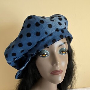 May include: A blue denim beret-style hat with large black polka dots. The hat has a brim and a rounded crown. The hat is worn by a mannequin with black hair and a neutral background.