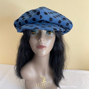 May include: A denim newsboy cap with black polka dots. The hat is displayed on a mannequin head with black hair. The mannequin has the text "HARLEM 125" on the chest.