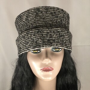 May include: A black and white knit hat with a brim. The hat has a horizontal striped pattern. The hat is made of a soft, textured material. The hat is shown on a mannequin with long black hair.