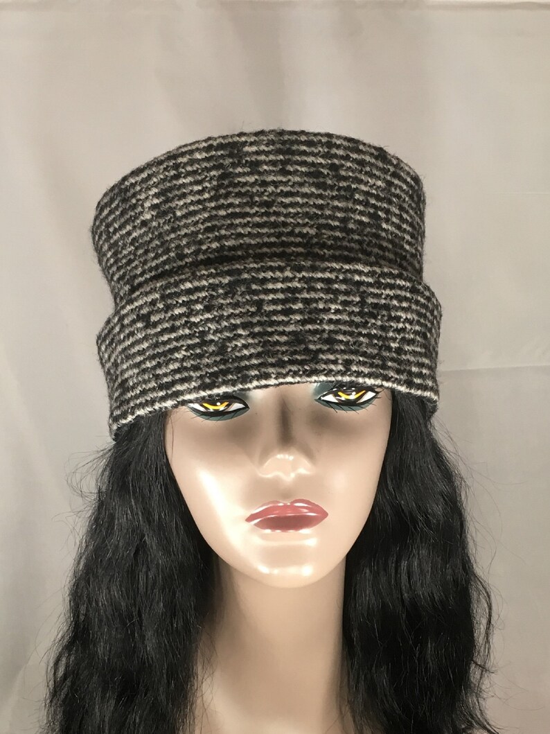 May include: A black and white knit hat with a brim. The hat has a horizontal striped pattern. The hat is made of a soft, textured material. The hat is shown on a mannequin with long black hair.