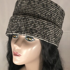 May include: A black and white patterned hat with a rectangular crown and a folded brim. The hat is made of a textured fabric and is displayed on a mannequin head with black hair.