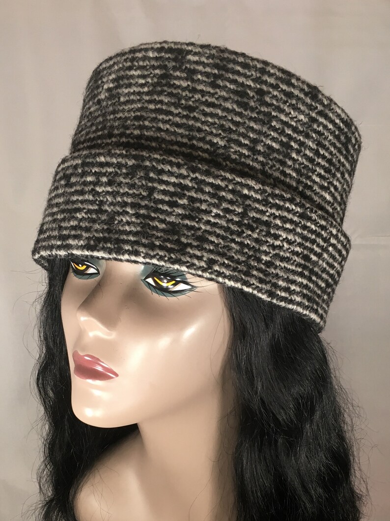 May include: A black and white patterned hat with a rectangular crown and a folded brim. The hat is made of a textured fabric and is displayed on a mannequin head with black hair.
