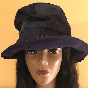 May include: A denim bucket hat with a dark blue crown and a wide, navy blue brim. The hat is constructed from various denim patches, creating a patchwork effect. The hat is displayed on a mannequin.