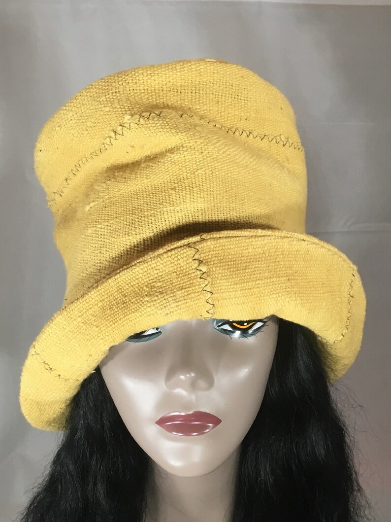 May include: A yellow bucket hat with a wide brim. The hat is made of a textured fabric and features visible stitching details. The hat is displayed on a mannequin head with black hair.