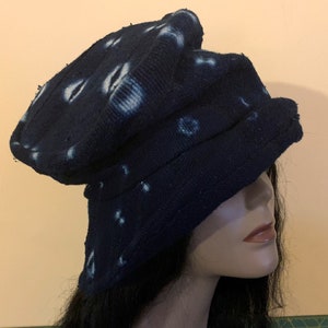 Puede incluir: Un sombrero azul oscuro con patrones circulares blancos. El sombrero est&aacute; hecho de una tela texturizada y tiene un dise&ntilde;o &uacute;nico y en capas. El sombrero se muestra en una cabeza de maniqu&iacute;.