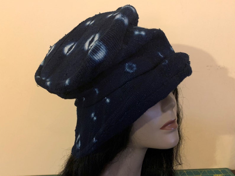 Puede incluir: Un sombrero azul oscuro con patrones circulares blancos. El sombrero est&aacute; hecho de una tela texturizada y tiene un dise&ntilde;o &uacute;nico y en capas. El sombrero se muestra en una cabeza de maniqu&iacute;.