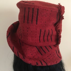 K&ouml;nnte beinhalten: Ein roter Stoffhut mit schwarzen vertikalen und gepunkteten Mustern. Der Hut hat einen gerollten Rand und einen Fransenrand. Der Hut besteht aus einem gewebten Material und scheint handgefertigt zu sein.