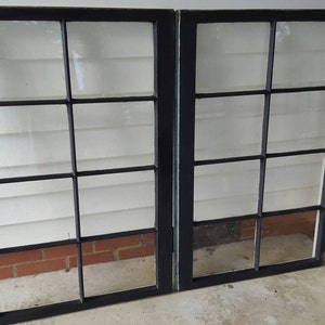 May include: Two black painted wooden windows with multiple panes of glass. The windows are closed and appear to be old.
