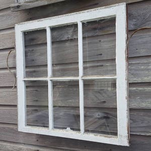 May include: A white painted wooden window with six panes of glass. The window is mounted on a weathered wooden wall.