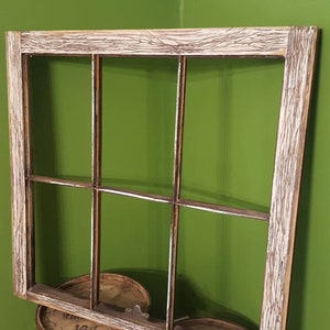 May include: A rustic wooden window frame with six panes of glass. The frame is painted white and has a distressed look. The window frame is sitting on top of two wooden barrels.