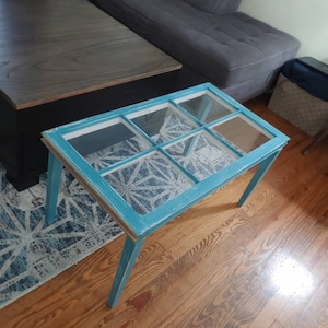 May include: A teal blue coffee table with a glass top and a white painted frame. The table has four legs and is made from reclaimed wood.