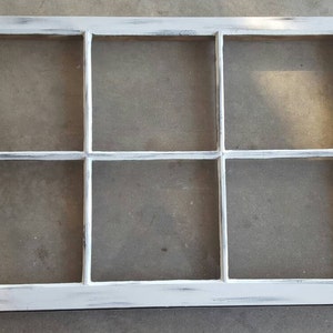 May include: A white painted wooden window frame with nine panes of glass. The frame has a distressed look with visible brushstrokes.