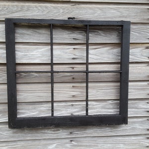 May include: A black wooden window frame with nine panes of glass. The frame is mounted on a wood wall.
