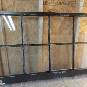 May include: A black painted wooden window frame with six panes of glass. The window frame has a distressed look with some of the black paint chipped off.