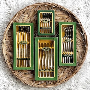 May include: Four boxes of Gense Swedish Stainless Steel silverware on a woven tray. Each green box contains multiple spoons or forks. The Gense logo is visible on each box. The tray is brown and circular.