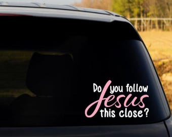 May include: A white and light pink vinyl decal applied to a dark car rear window. The decal features the text "Do you follow" in white, the word "Jesus" in a large, cursive light pink font, and the text "this close?" in white lettering.