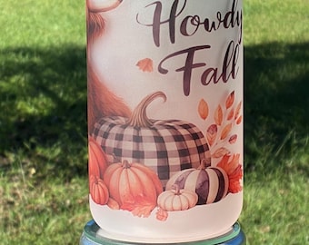 May include: A frosted glass tumbler with a bamboo lid featuring a graphic of a Highland cow, pumpkins, and autumn leaves. The text "Howdy Fall" is printed in dark brown script. The glass has a cylindrical shape and a smooth, matte finish.