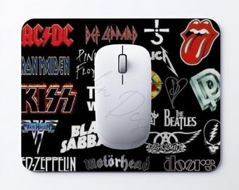 May include: A rectangular black mousepad featuring a collage of various rock band logos including AC/DC, Def Leppard, The Rolling Stones, Kiss, and The Beatles, with a plain white computer mouse resting on top of the surface.