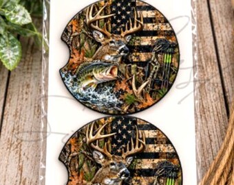 May include: Two circular car coasters in clear packaging labeled Car Coasters. The design features a deer, a fish, and a compound bow over a camouflage American flag background. The coasters have a notch on the left side for easy removal.