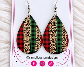 May include: Teardrop-shaped earrings featuring a vertical pattern of red and black buffalo plaid, leopard print, and green and black buffalo plaid. The earrings are displayed on a white card with the text @simplicustomdesigns and social media icons.