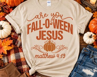 May include: A beige short-sleeved t-shirt featuring orange text that reads are you FALL-O-WEEN JESUS and matthew 4:19, with a central orange pumpkin graphic and decorative swirls printed on the front of the garment.