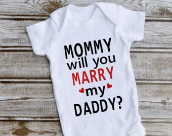 May include: A white short-sleeved baby bodysuit featuring the black text MOMMY will you, the red text MARRY, two small red hearts, and the black text my DADDY? printed on the front. The garment includes a round neckline and three snap closures.