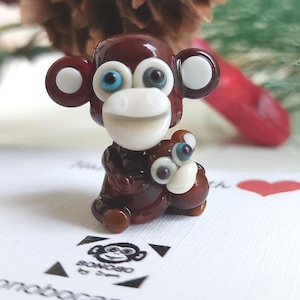 May include: A brown glass monkey figurine holding a smaller brown glass monkey figurine. Both monkeys have white faces and blue eyes.