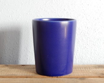 May include: A deep blue ceramic cup or mug. The cup is sitting on a wooden surface.
