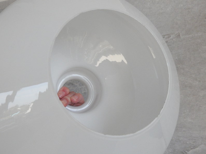 May include: White ceramic lampshade with a round opening in the center. The opening is large enough for a hand to fit through.