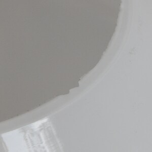 May include: Close-up of a white ceramic lampshade with a slightly chipped edge.