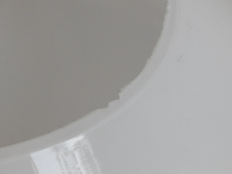 May include: Close-up of a white ceramic lampshade with a slightly chipped edge.