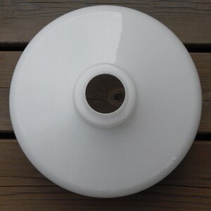 May include: White enamel lampshade with a round shape and a hole in the center. The lampshade is on a wooden surface.