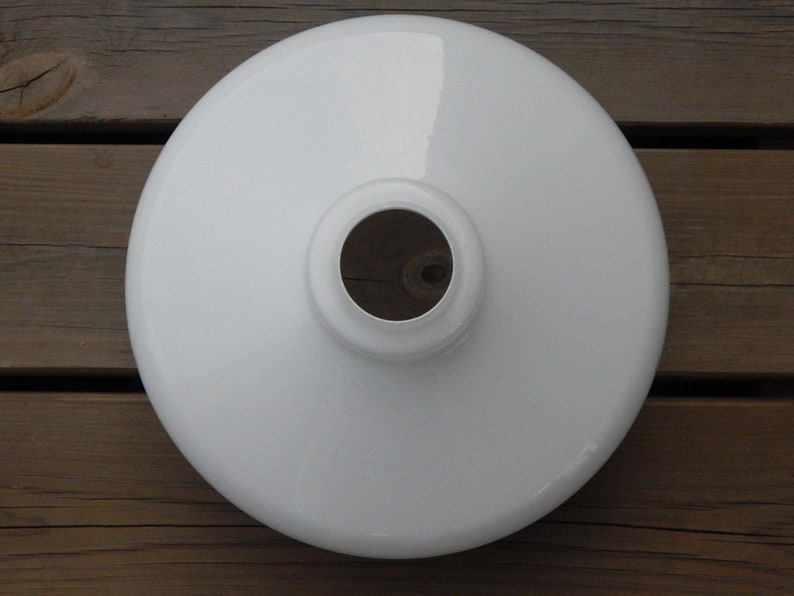 May include: White enamel lampshade with a round shape and a hole in the center. The lampshade is on a wooden surface.