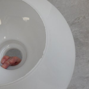 May include: White ceramic lampshade with a round opening at the top. The opening is large enough for a hand to fit through.