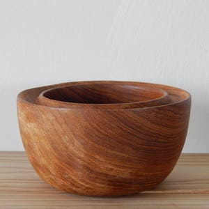 Puede incluir: Dos cuencos de madera, uno anidado dentro del otro. Los cuencos est&aacute;n hechos de madera marr&oacute;n oscura con un patr&oacute;n de veta natural.